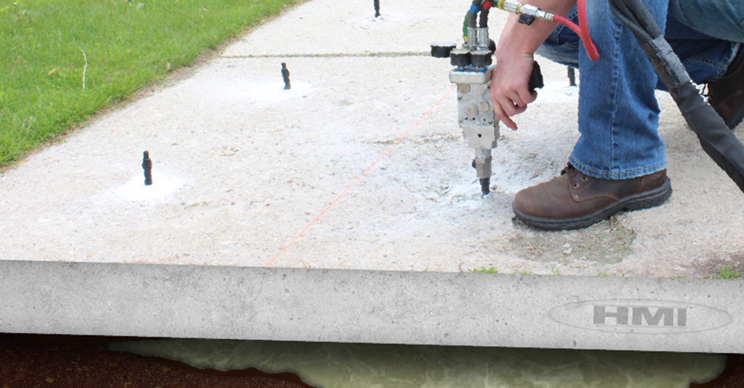 A person is using a drill on a concrete surface with an HMI logo in the background.